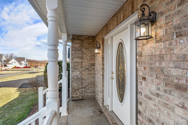 view of exterior entry featuring a porch and brick siding