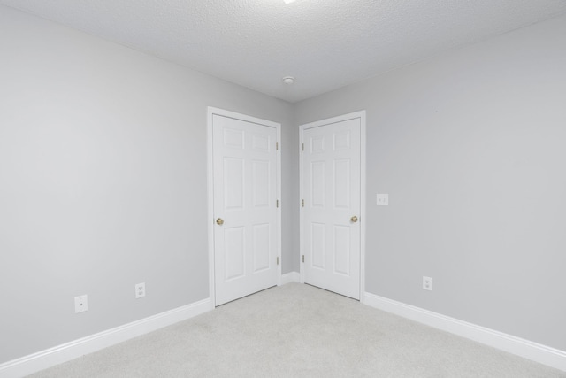 unfurnished bedroom with light carpet, a textured ceiling, and baseboards