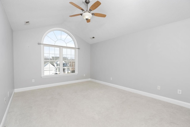 empty room with light colored carpet, visible vents, a ceiling fan, vaulted ceiling, and baseboards