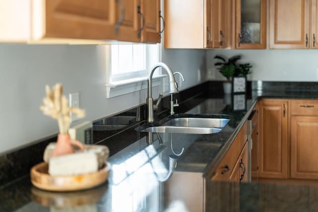 kitchen featuring dark stone counters, brown cabinetry, a sink, and glass insert cabinets