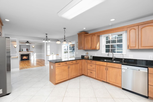 kitchen with a warm lit fireplace, appliances with stainless steel finishes, open floor plan, a peninsula, and a sink