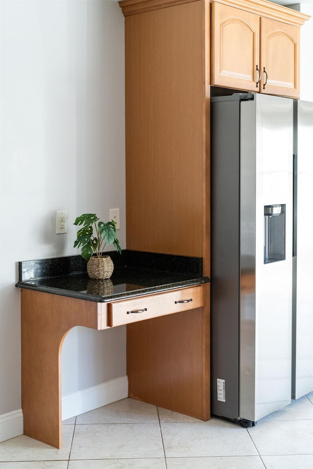 kitchen featuring dark stone counters, light brown cabinetry, light tile patterned floors, and stainless steel fridge