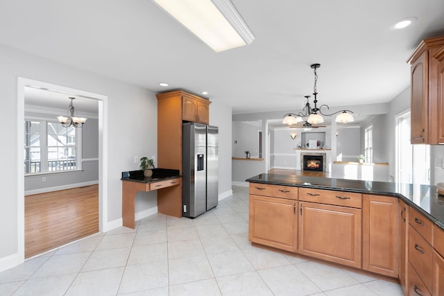 kitchen featuring dark countertops, a peninsula, a lit fireplace, a chandelier, and stainless steel refrigerator with ice dispenser