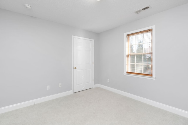 spare room featuring baseboards, a textured ceiling, visible vents, and light colored carpet