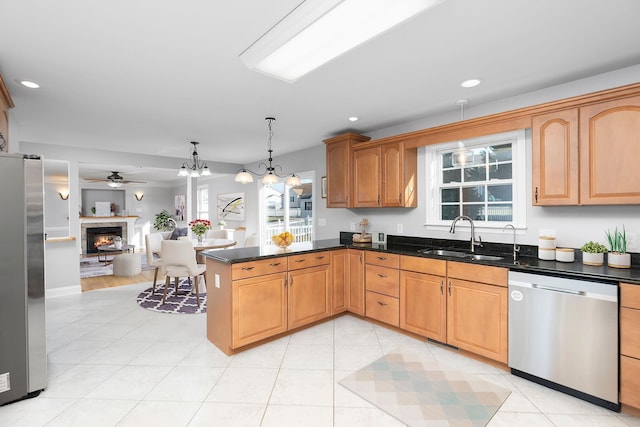 kitchen with a warm lit fireplace, a peninsula, a sink, open floor plan, and appliances with stainless steel finishes