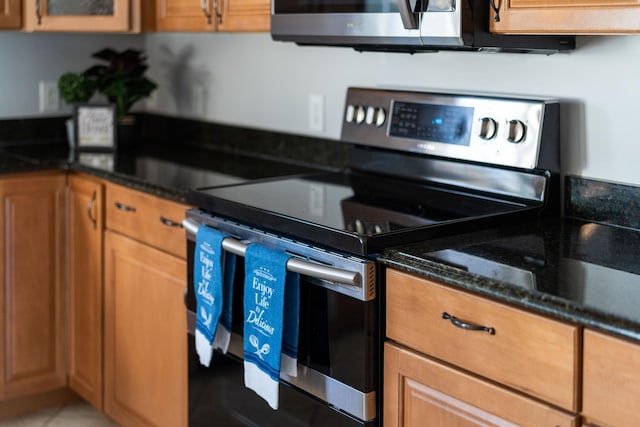 kitchen featuring dark stone counters, appliances with stainless steel finishes, brown cabinetry, and glass insert cabinets