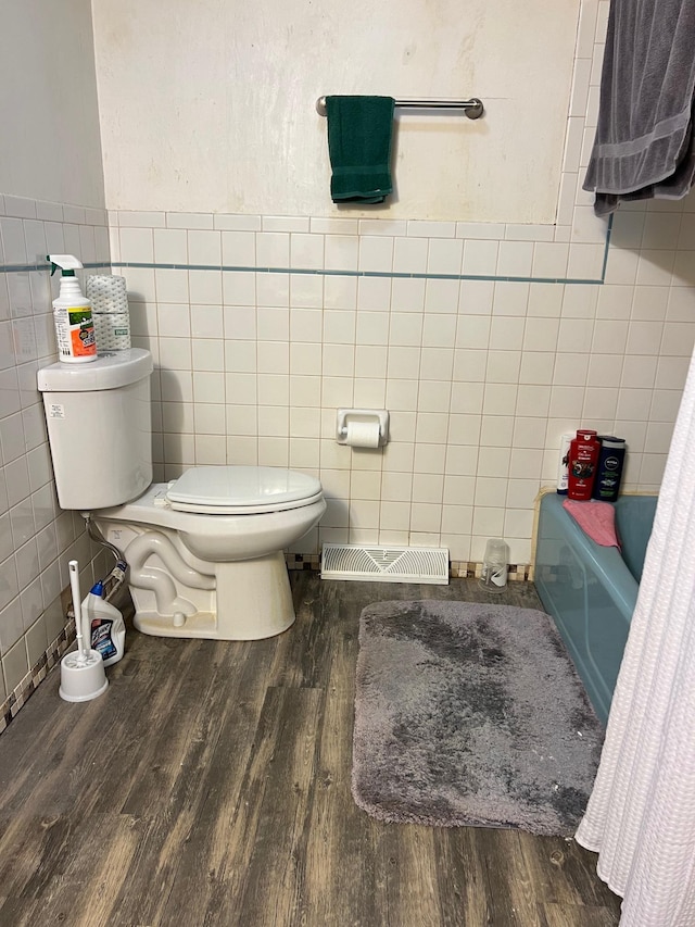 bathroom featuring shower / bathtub combination with curtain, wood-type flooring, toilet, and tile walls