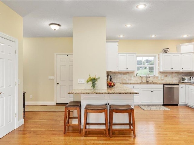 kitchen with a kitchen bar, sink, dishwasher, kitchen peninsula, and white cabinets