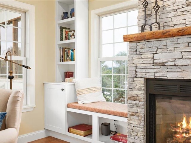 sitting room with a stone fireplace, hardwood / wood-style floors, and built in shelves