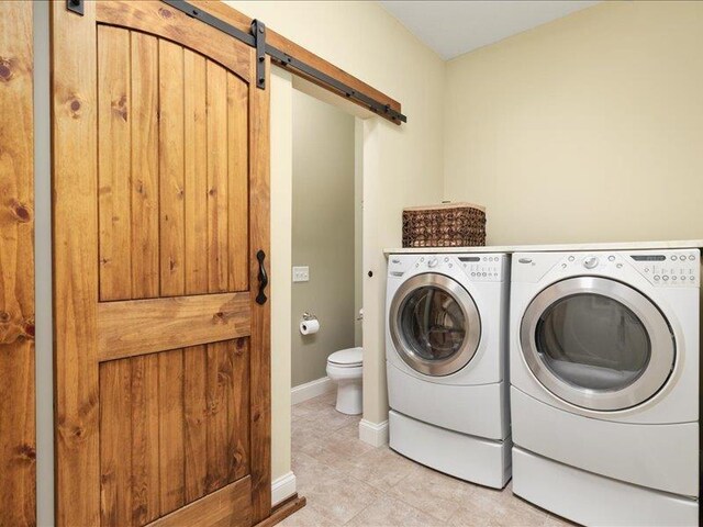 laundry room with light tile patterned flooring, a barn door, and washer and dryer