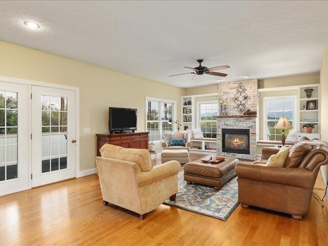 living room with ceiling fan, a stone fireplace, and light hardwood / wood-style flooring