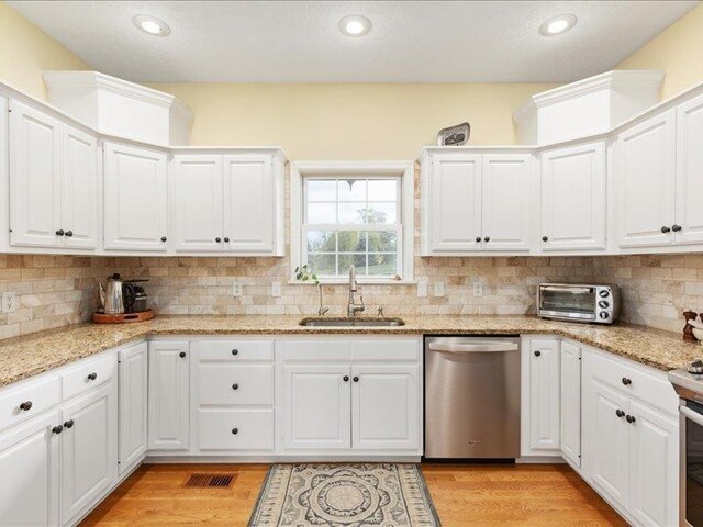 kitchen featuring white cabinetry, sink, stainless steel dishwasher, and light stone countertops