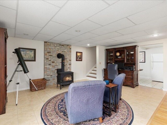 living room featuring light tile patterned flooring, a wood stove, and a drop ceiling