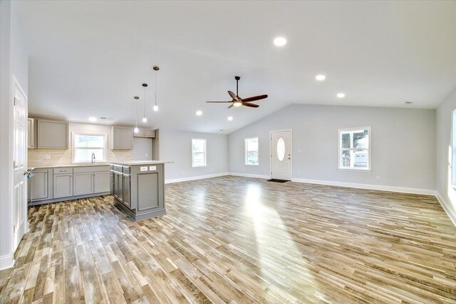 kitchen featuring pendant lighting, lofted ceiling, gray cabinetry, backsplash, and light hardwood / wood-style floors