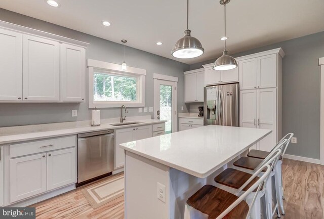 kitchen with a center island, a kitchen bar, white cabinets, stainless steel appliances, and a sink