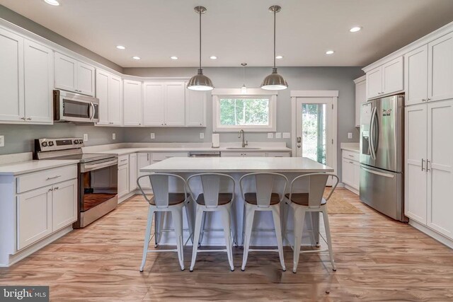 kitchen with a kitchen island, a breakfast bar, a sink, stainless steel appliances, and white cabinetry