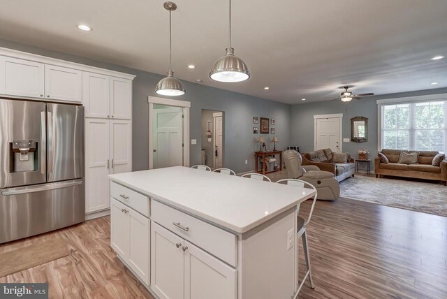 kitchen featuring a breakfast bar, a ceiling fan, a center island, stainless steel fridge, and light wood finished floors