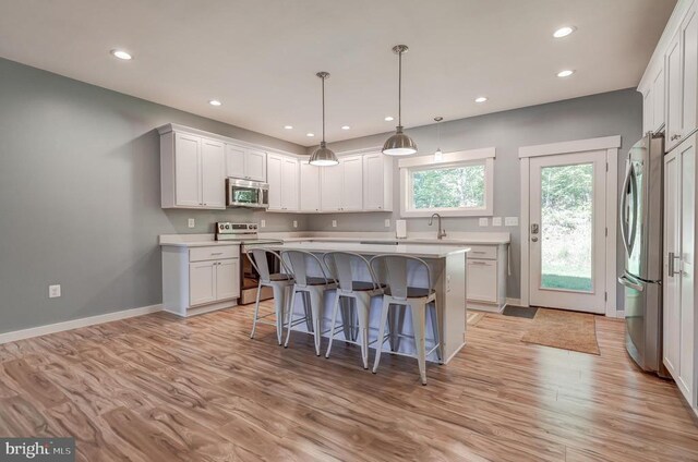 kitchen featuring a kitchen bar, a sink, light wood-style floors, appliances with stainless steel finishes, and light countertops