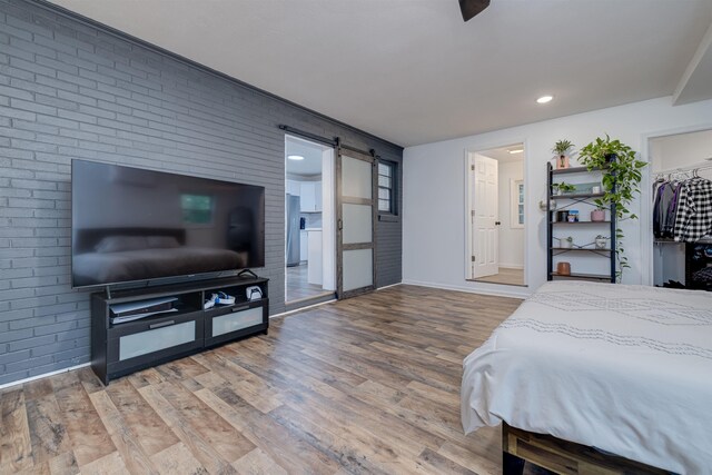 bedroom featuring wood-type flooring, a barn door, and brick wall