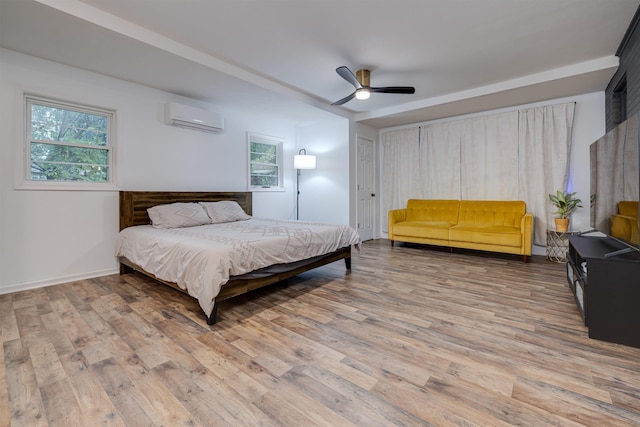 bedroom with ceiling fan, hardwood / wood-style floors, multiple windows, and an AC wall unit