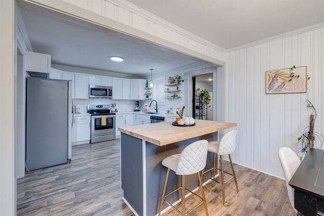 kitchen featuring pendant lighting, stainless steel appliances, a kitchen breakfast bar, white cabinets, and wood counters