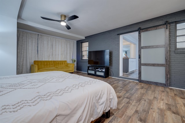 bedroom featuring ceiling fan, brick wall, a barn door, and wood-type flooring