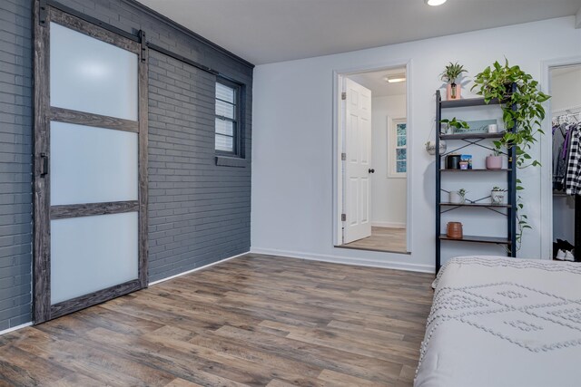 bedroom featuring a barn door, brick wall, and dark hardwood / wood-style flooring