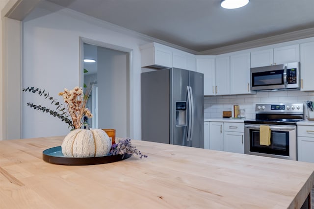 kitchen featuring stainless steel appliances, white cabinetry, ornamental molding, and tasteful backsplash