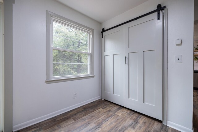 unfurnished bedroom featuring a barn door, dark hardwood / wood-style flooring, and a closet