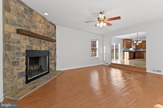 unfurnished living room with ceiling fan with notable chandelier, a fireplace, and light hardwood / wood-style floors