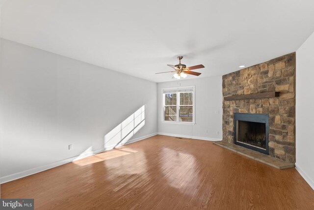 unfurnished living room featuring a stone fireplace, ceiling fan, and hardwood / wood-style flooring