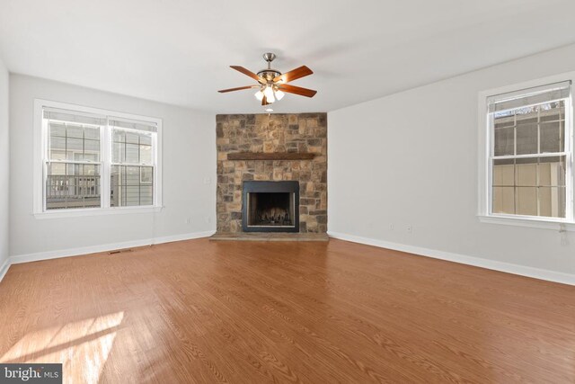 unfurnished living room with ceiling fan, wood-type flooring, and a stone fireplace