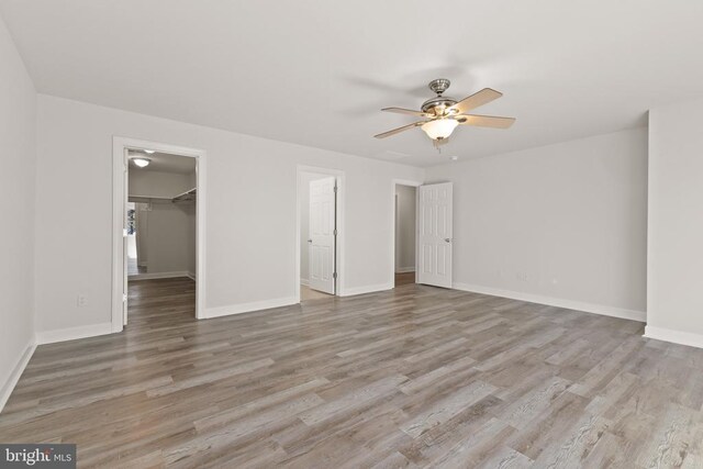 unfurnished bedroom featuring ceiling fan, a spacious closet, light wood-type flooring, and a closet