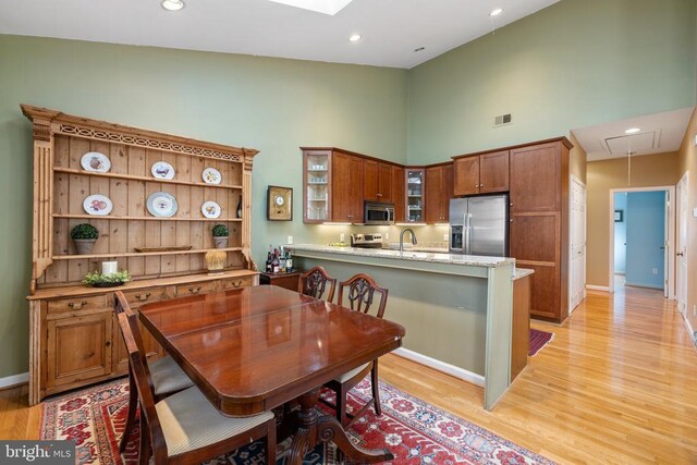 dining area with sink, high vaulted ceiling, and light hardwood / wood-style flooring