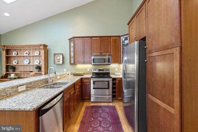 kitchen with lofted ceiling, sink, appliances with stainless steel finishes, kitchen peninsula, and light stone countertops