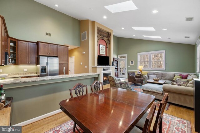 dining space with a skylight, high vaulted ceiling, and light hardwood / wood-style flooring