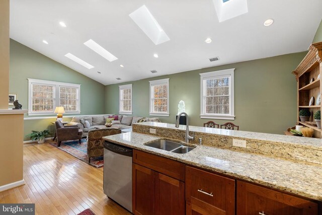 kitchen with sink, vaulted ceiling with skylight, light stone counters, light hardwood / wood-style floors, and stainless steel dishwasher