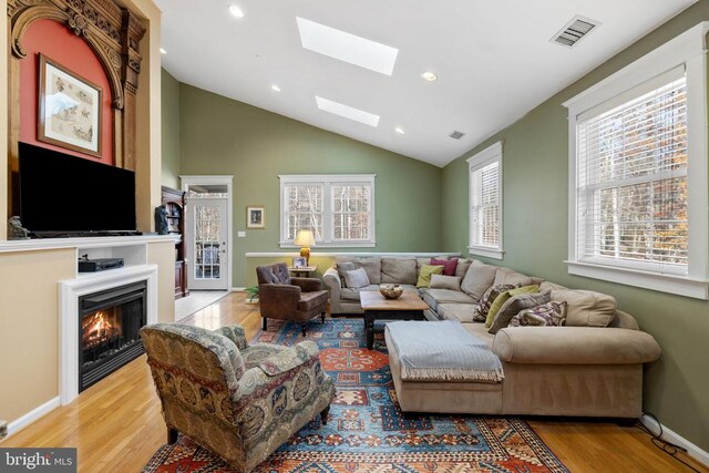 living room with lofted ceiling with skylight and light wood-type flooring