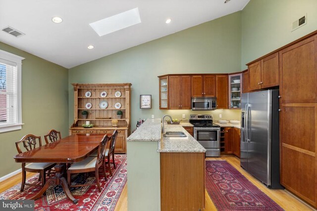 kitchen featuring sink, a skylight, stainless steel appliances, light stone countertops, and kitchen peninsula