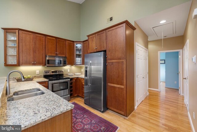 kitchen with sink, stainless steel appliances, a high ceiling, light stone counters, and light wood-type flooring