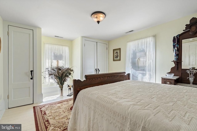 bedroom with light wood finished floors, visible vents, and a closet