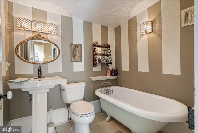 bathroom featuring baseboards, a soaking tub, wood finished floors, and toilet