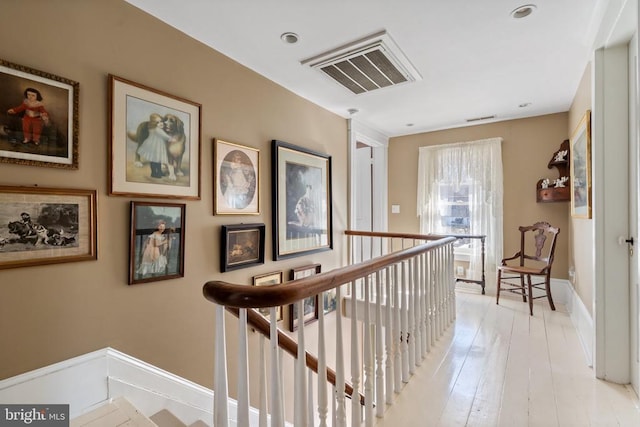 hallway with visible vents, an upstairs landing, baseboards, and light wood-style flooring