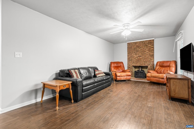 living area with baseboards, a wood stove, ceiling fan, hardwood / wood-style flooring, and a textured ceiling