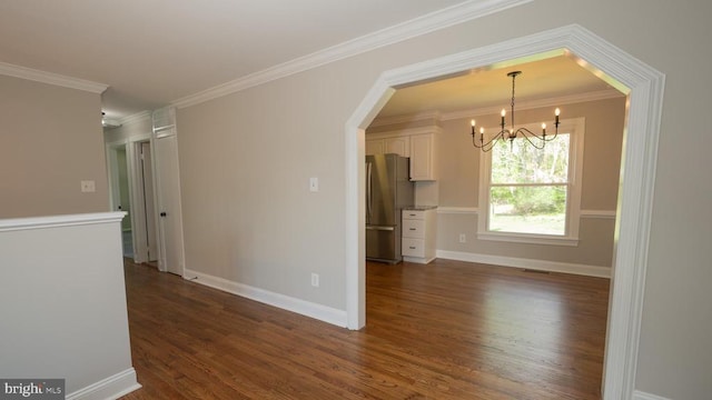 spare room featuring crown molding, an inviting chandelier, arched walkways, baseboards, and dark wood-type flooring