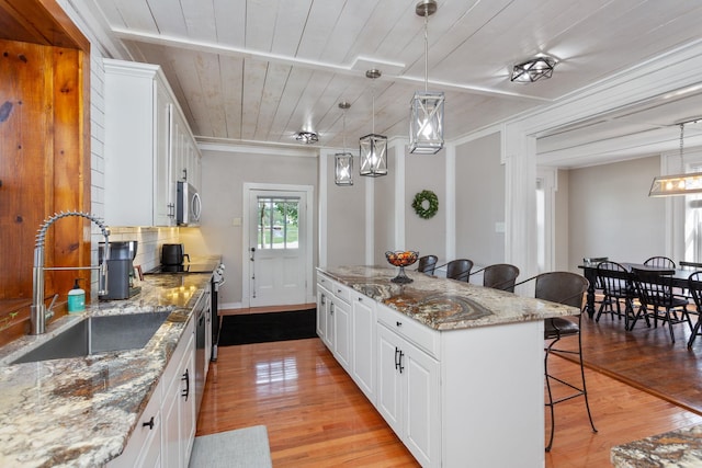 kitchen featuring a breakfast bar area, a kitchen island, appliances with stainless steel finishes, a sink, and light wood finished floors