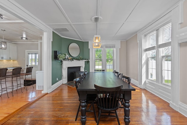 dining area with wood-type flooring, a fireplace with flush hearth, a wealth of natural light, and visible vents