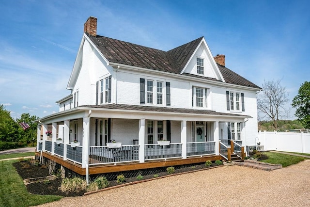 farmhouse with covered porch, fence, and a chimney
