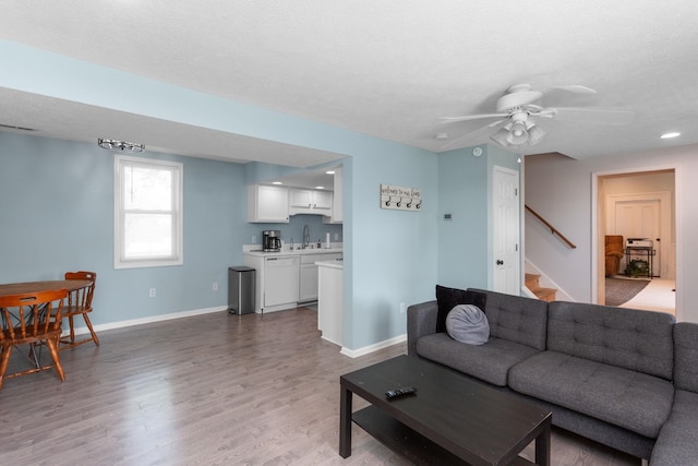 living room featuring ceiling fan, baseboards, stairway, and light wood-style floors
