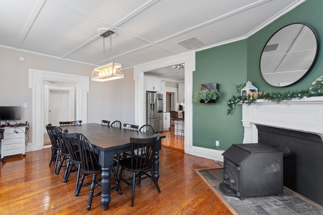 dining area with visible vents, a wood stove, wood finished floors, and ornamental molding